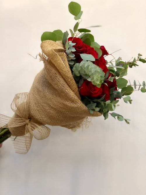 A dozen red roses in a wrapped organic bouquet with eucalyptus